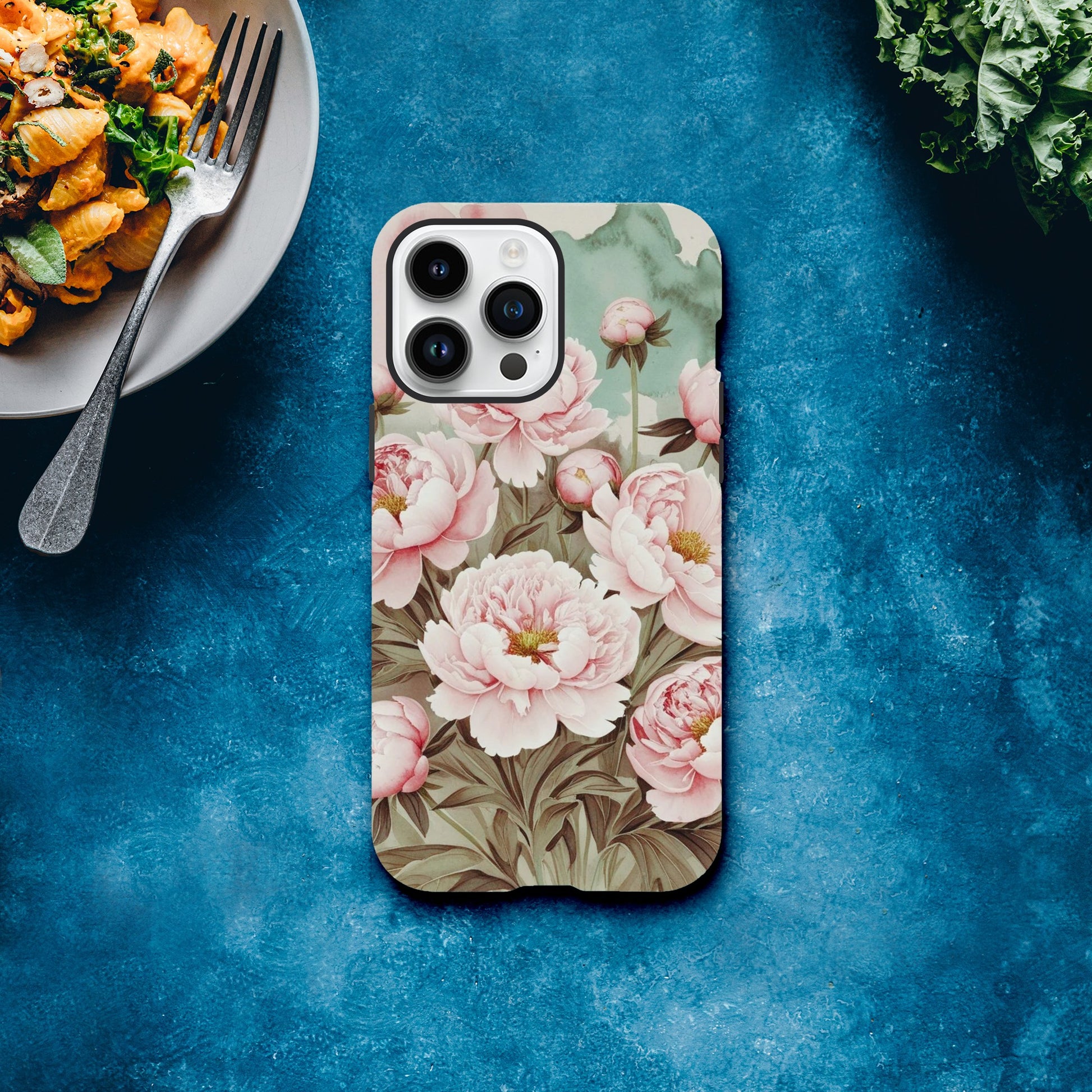 Protect your iPhone in style with a dual-layer tough case featuring pink peonies on a mint green background. Fits iPhone 12+ and supports wireless charging.