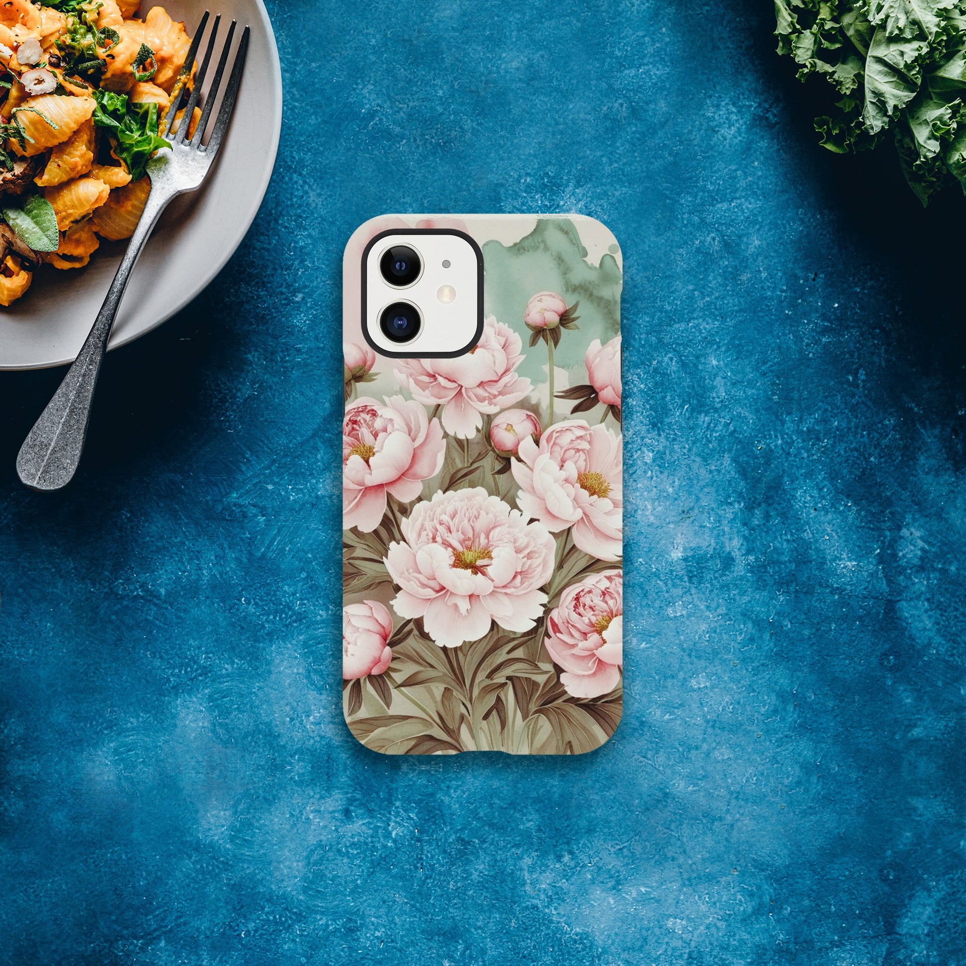 Protect your iPhone in style with a dual-layer tough case featuring pink peonies on a mint green background. Fits iPhone 12+ and supports wireless charging.